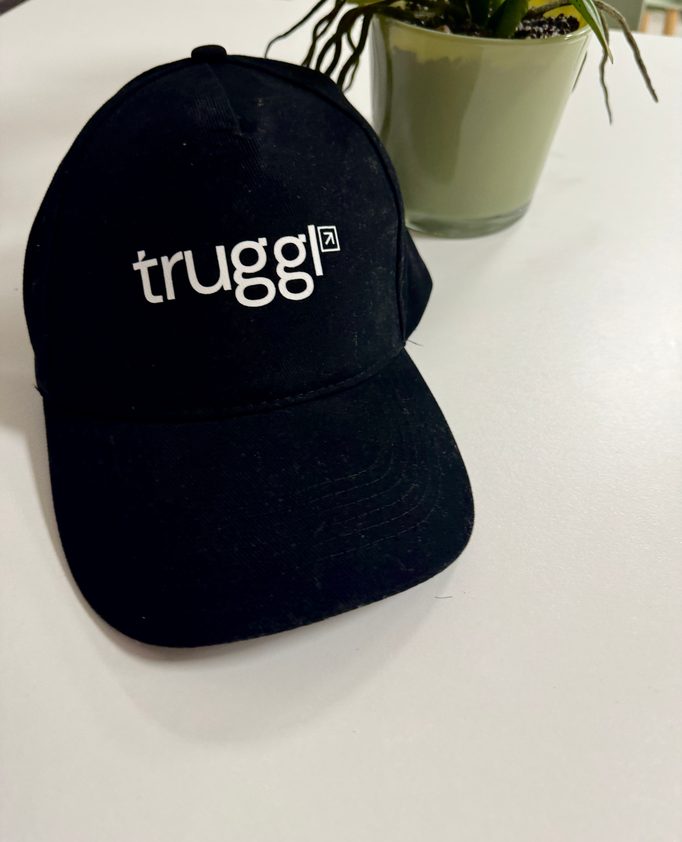 A black Truggl cap on a white desk beside a potted plant