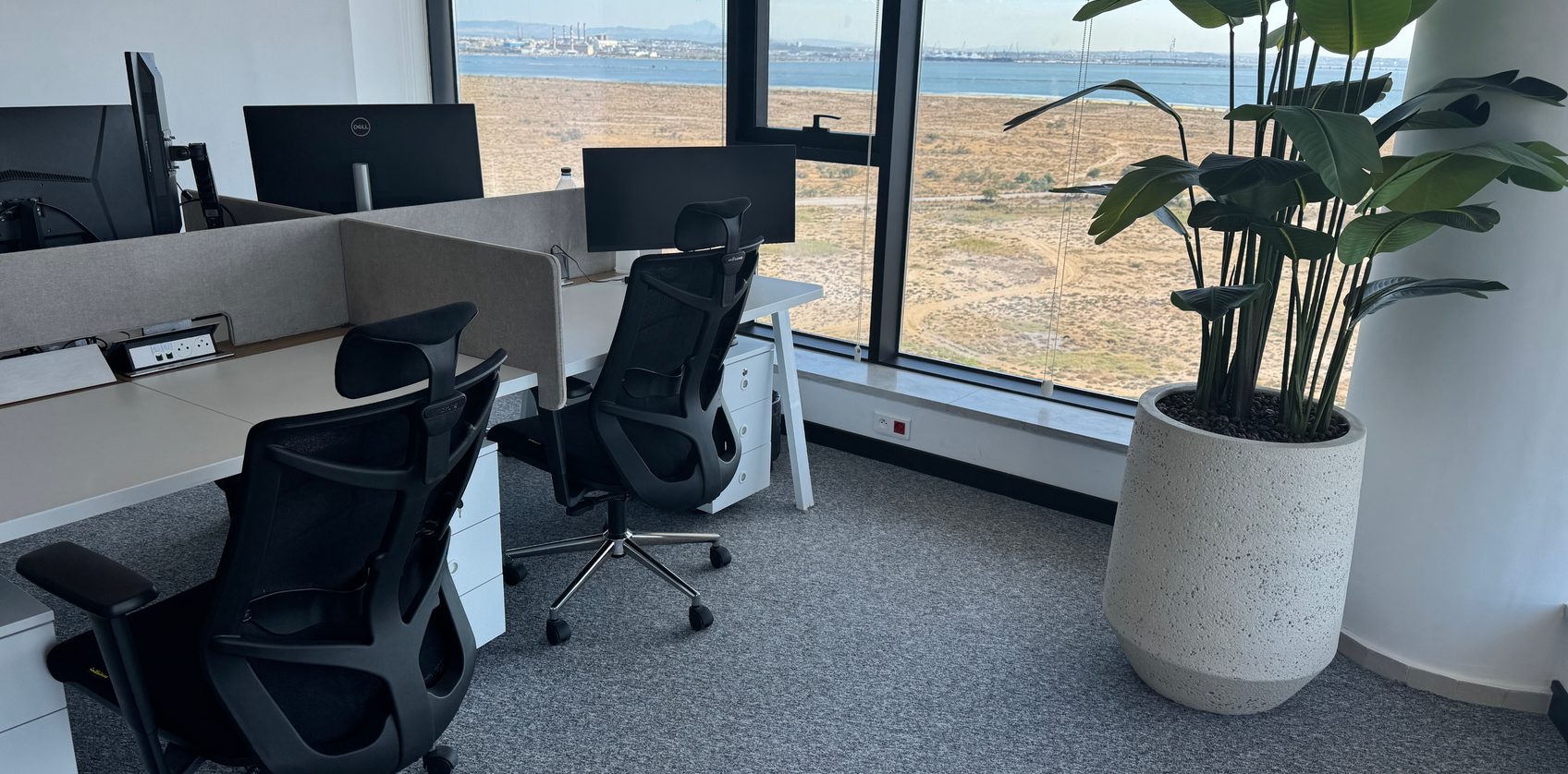 Empty desks and monitors by a window looking out over the coast
