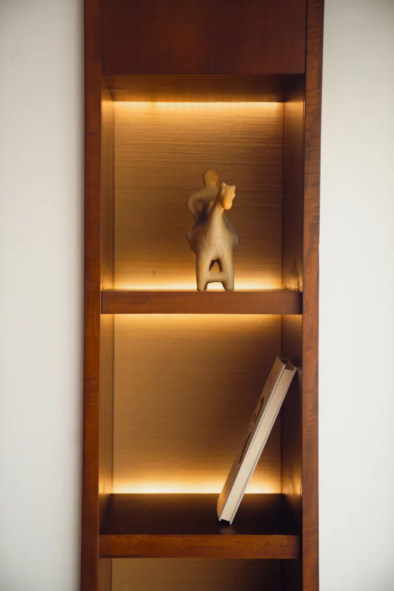 A carved figure and a book on a lit wooden shelf