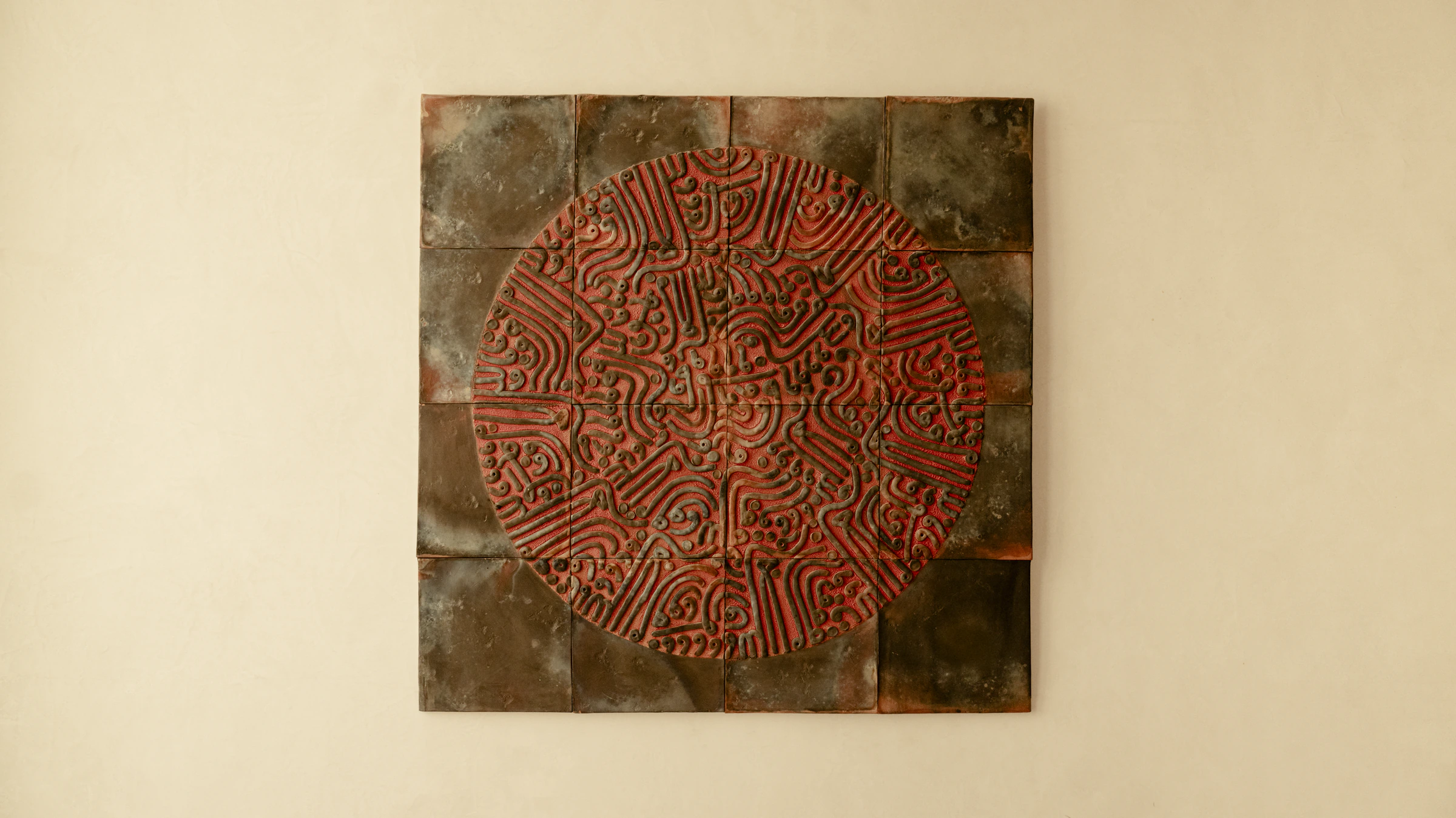 A wall panel of glazed tiles, a red circle of raised winding lines at its centre